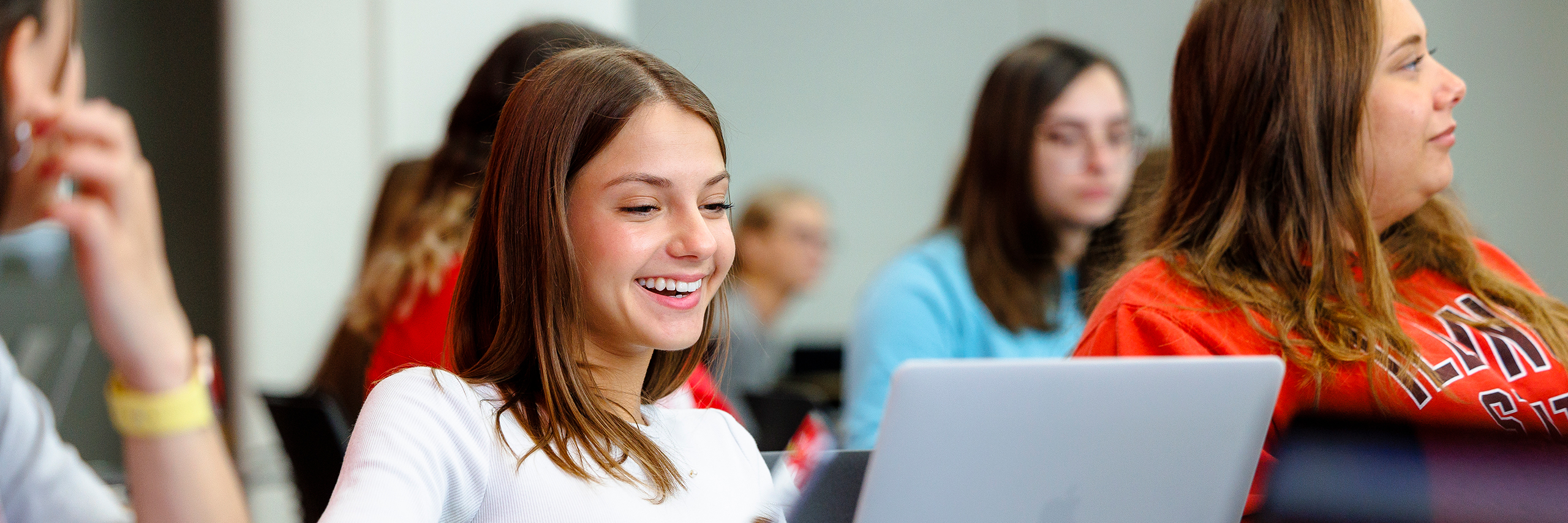 Student looking to a laptop screen and smiling in classroom.