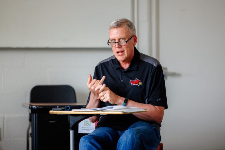 Jeff Klepec gestures while speaking in class at a desk